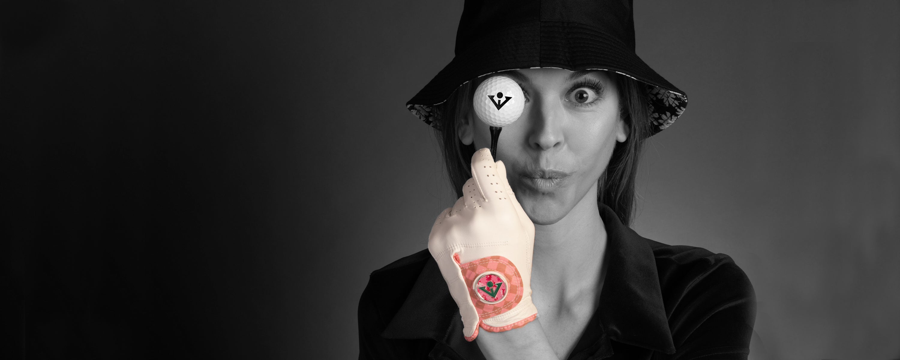 Woman making a fun face while holding up a tee with a VivanTee logo golf ball wearing the best womens golf glove in white and pink.