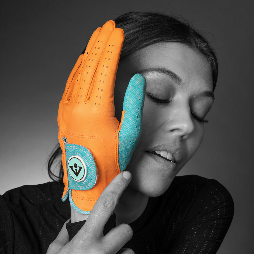 Orange women's golf glove across a models face in a pose looking down, featured in a monochromatic setting.