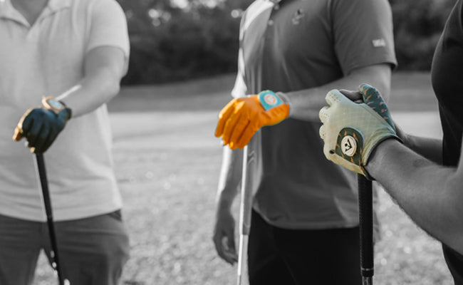 Group of 3 golfers wearing different colored golf gloves with ball markers standing around in a circle, holding their clubs in a monochromatic setting.
