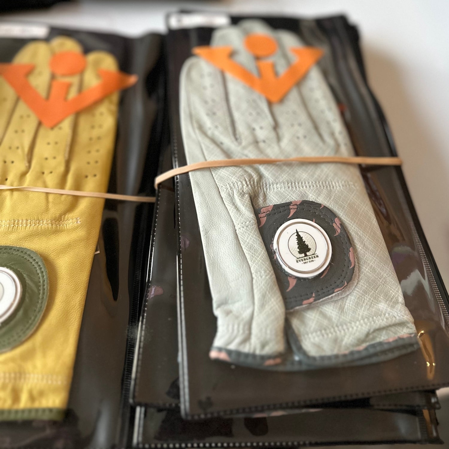 Batch of wholesale golf gloves with magnetic ball markers close up, logo showing on ball marker as "Evergreen Golf Club".