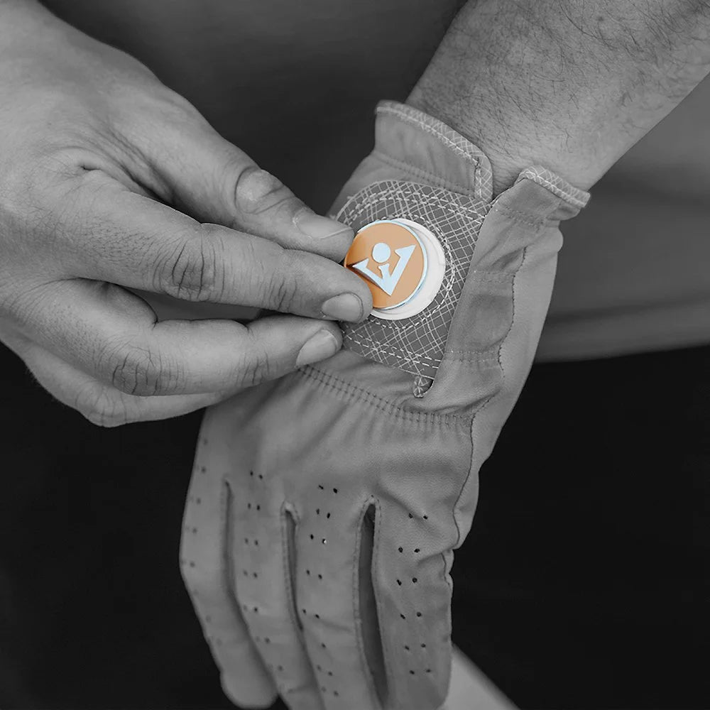 Man switching out his magnetic ball marker on his golf glove, with the magnetic ball marker in orange and silver VivanTee logo and the rest of the image in black and white.