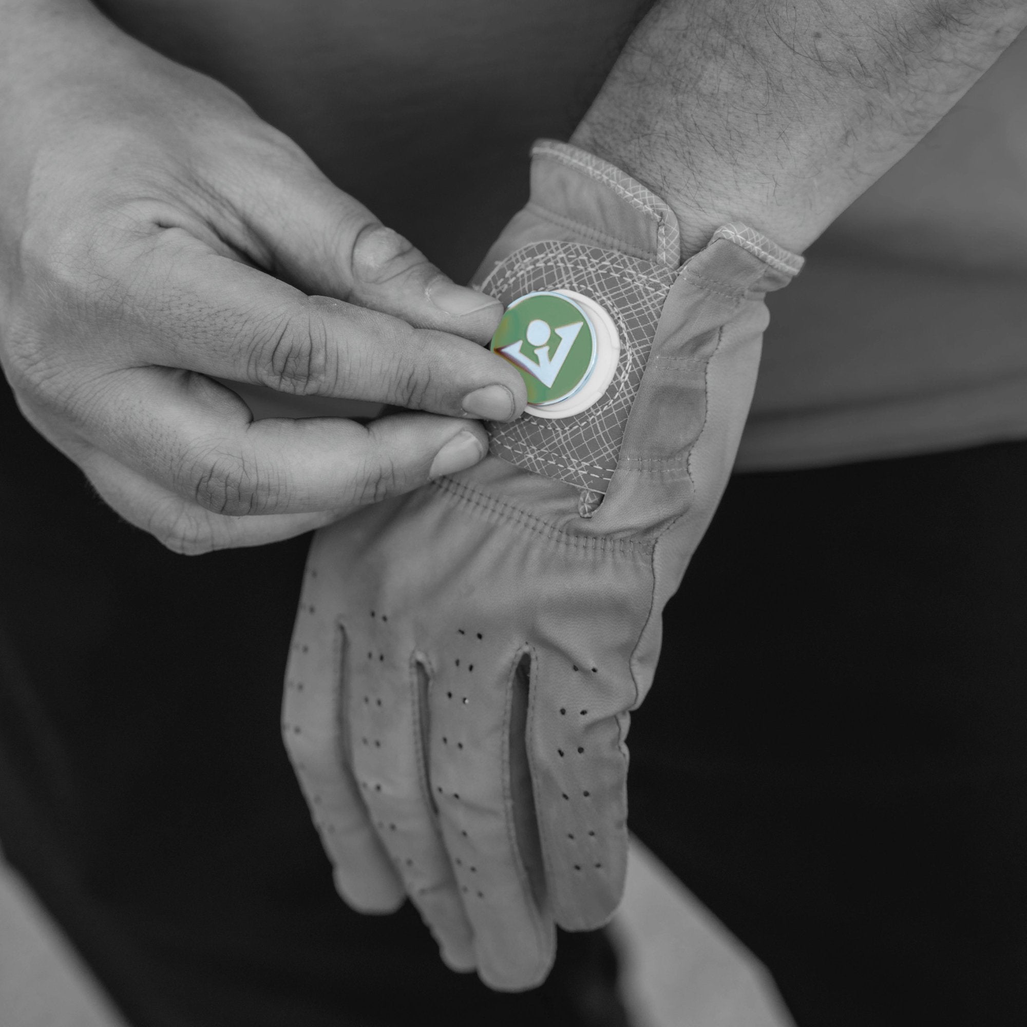 Man switching out his magnetic ball marker on his golf glove, with the magnetic ball marker in green and a VivanTee logo and the rest of the image in black and white.