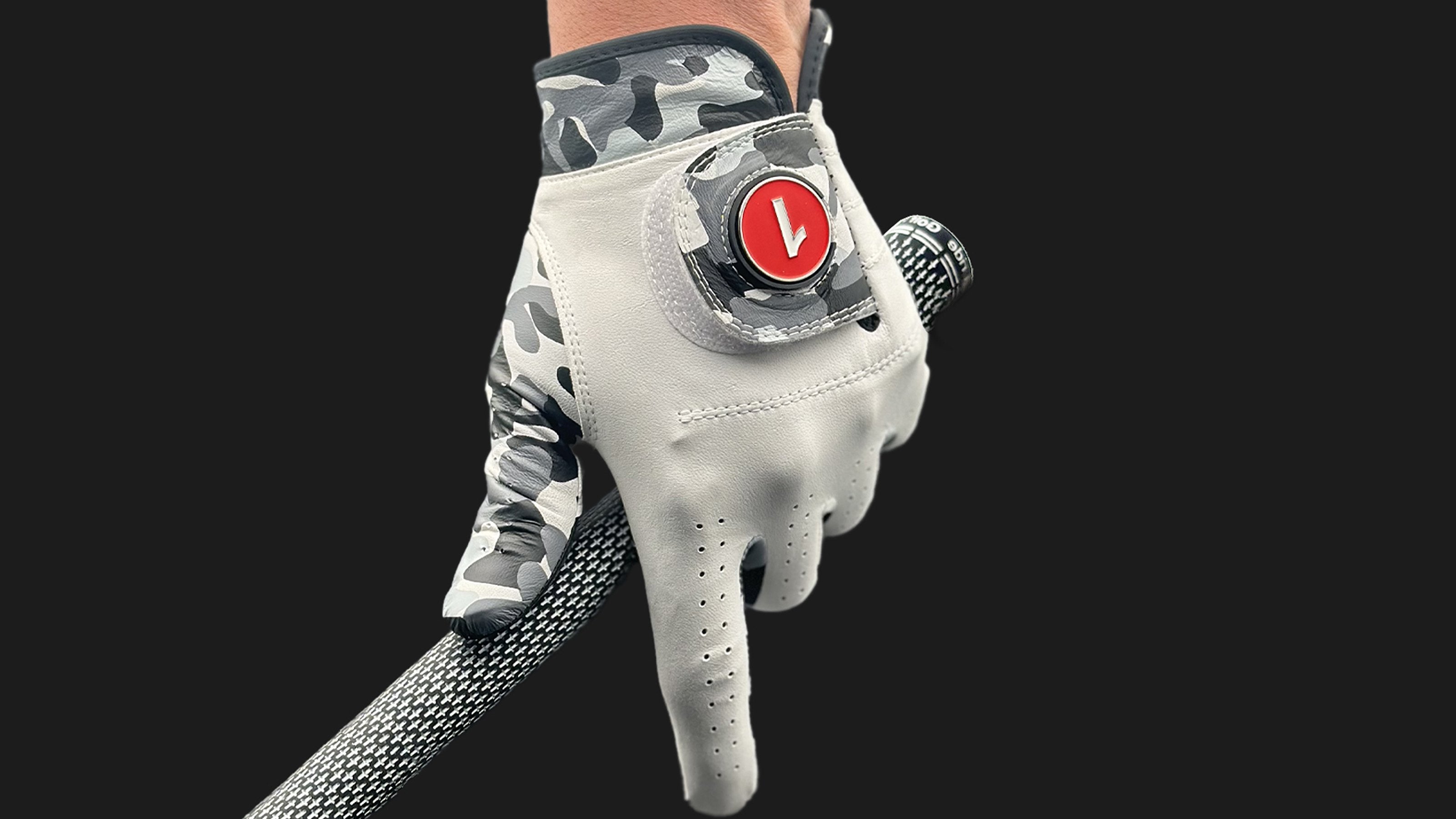 Image of a unique golf glove in camo with ball marker in red up close and a black background holding a golf club.