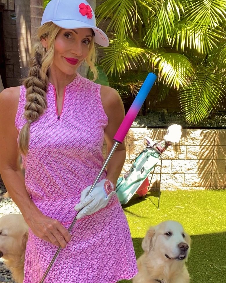 Fashionable female golfer in all pink and wearing a pink fancy golf glove with magnetic ball marker, posing next to a dog.