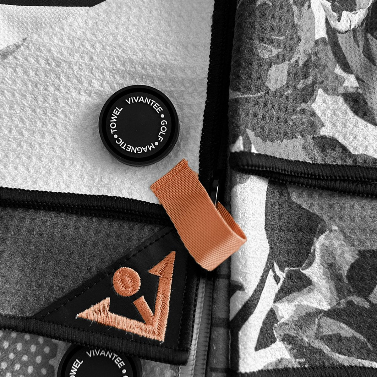 Close up of VivanTee's magnetic golf towel silicone logo in black and white titled "VIVANTEE GOLF MAGNETIC TOWEL", with the only color being the embroidered logo and latch tab in orange.  