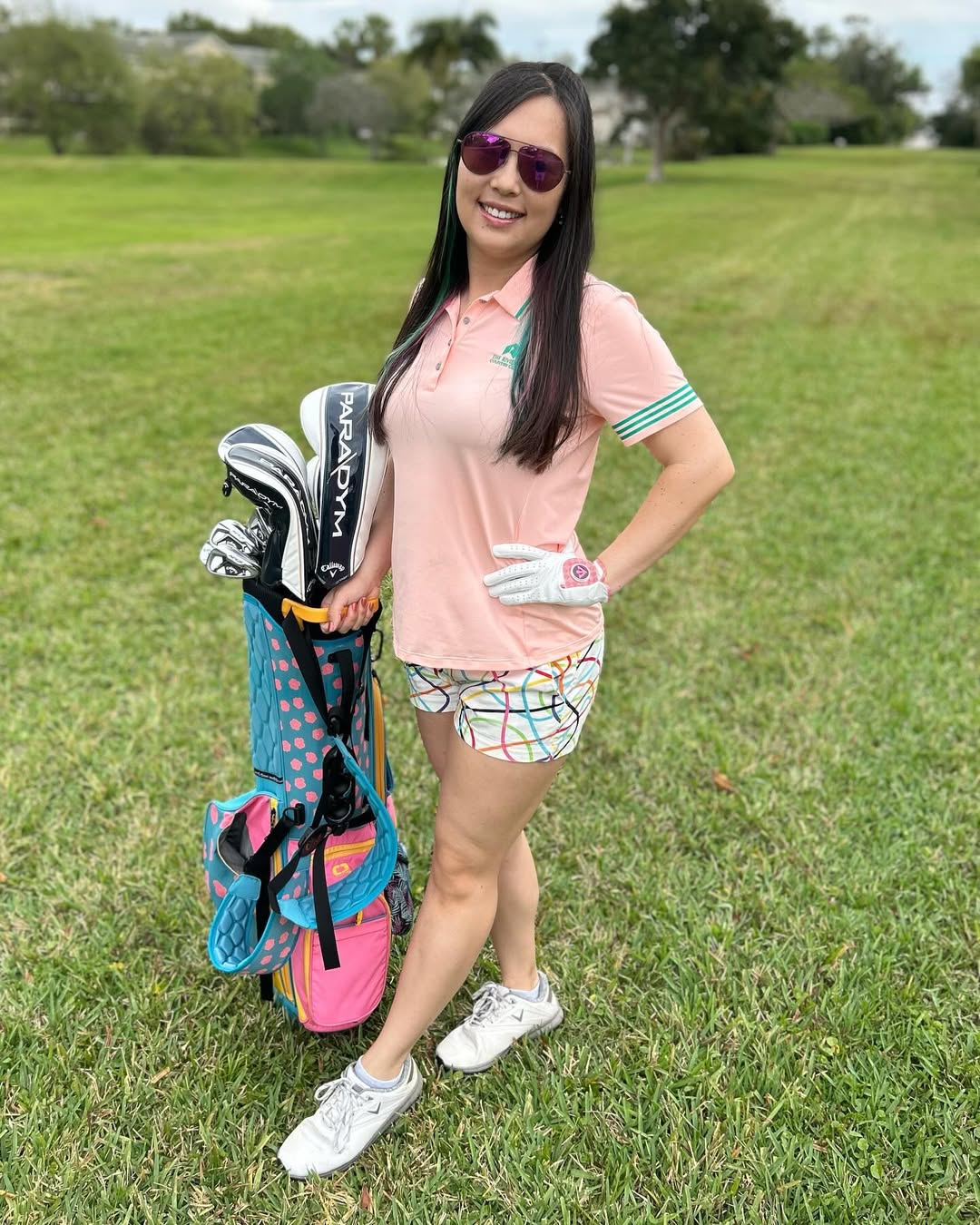 A female golfer poses on the fairway, holding her golf bag while wearing a stylish pink golf glove. This women's fancy golf glove blends high-end design with performance, creating a statement piece for the modern golfer."