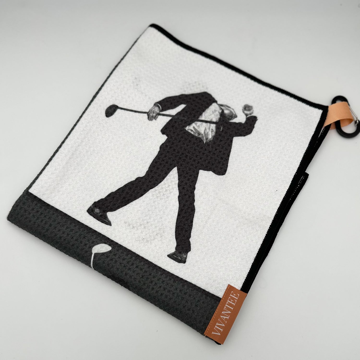 Magnetic golf towel featuring a grayscale image of a male golfer mid-swing, printed on a textured black fabric. A tan loop with a black carabiner provides practical functionality, while a sleek magnetic marker labeled "VIVANTEE GOLF • MAGNETIC • TOWEL" enhances the premium aesthetic. 