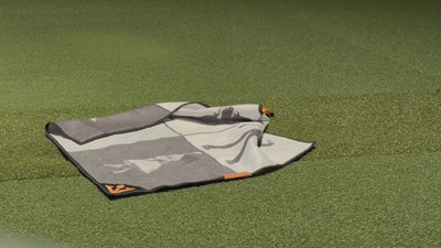 Video of VivanTee magnetic golf towel in black, white, and orange on the ground and being picked up by a golfer with their golf club.