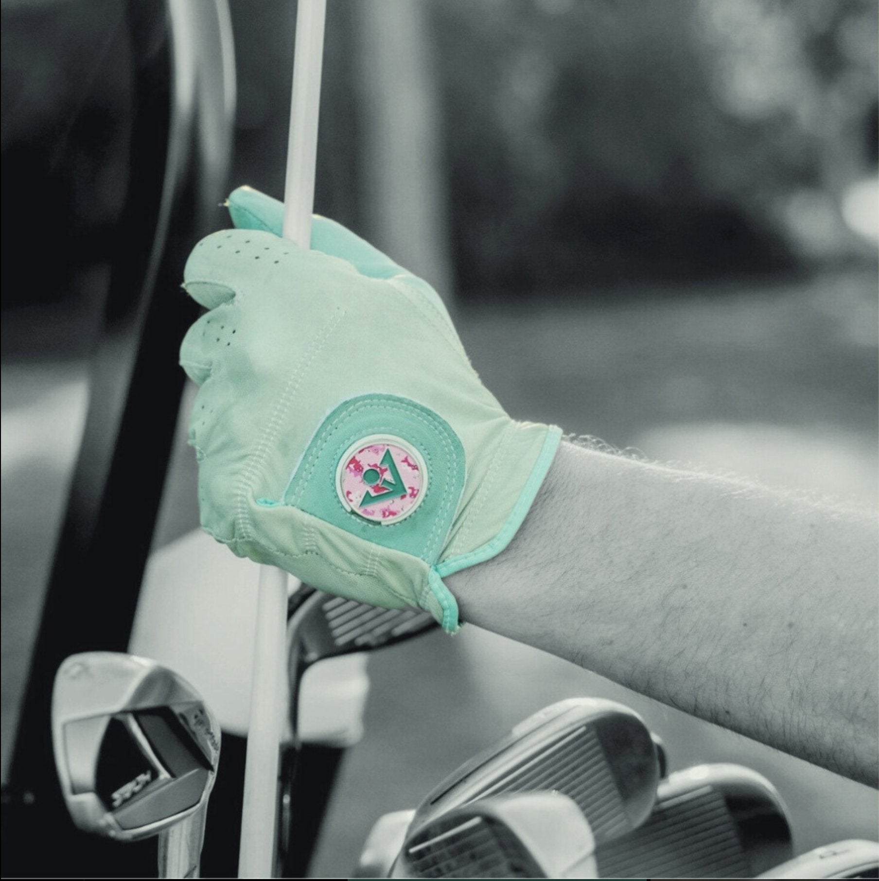 A unique golf glove with pink camo ball marker putting a driver away in a golf bag with a black and white background.