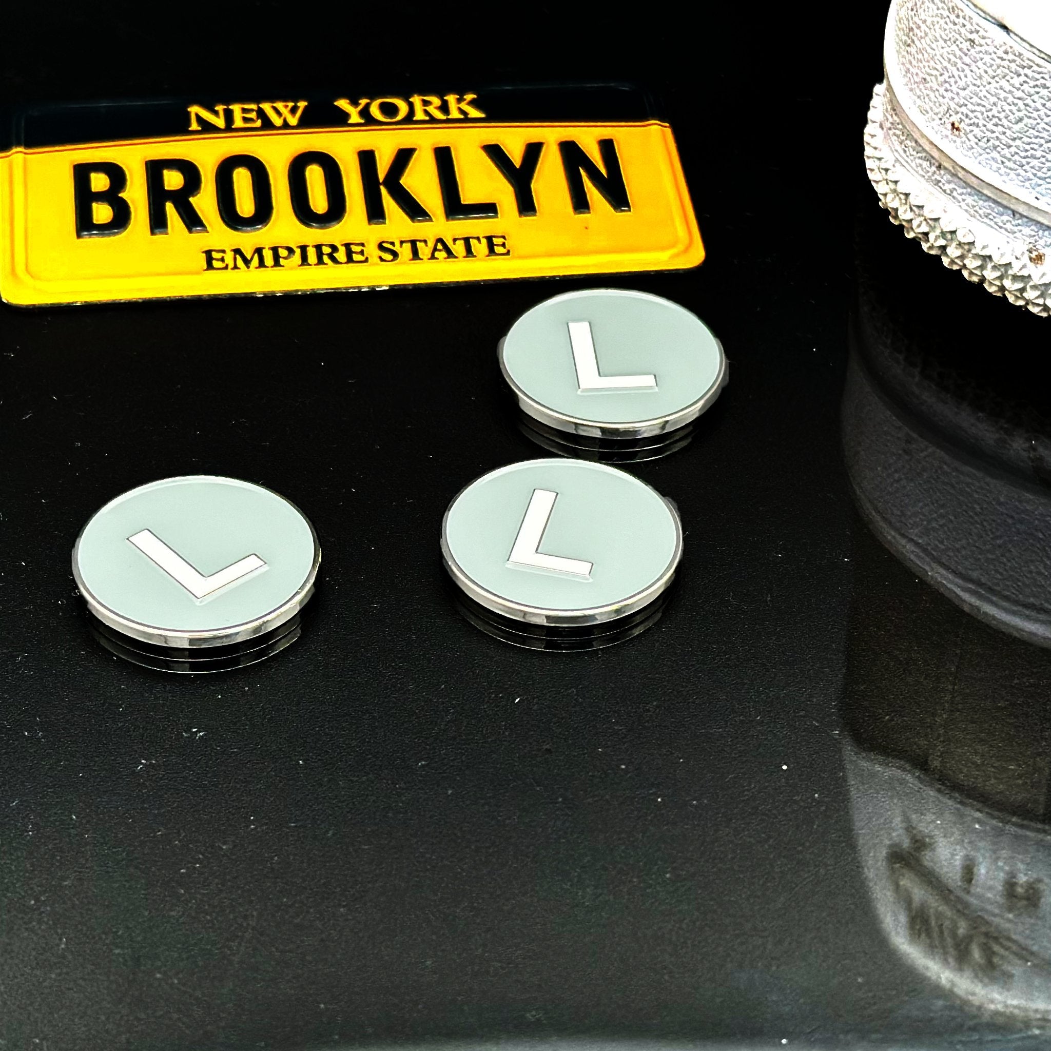 L Train Fun Magnetic Golf Ball Marker next to a Brooklyn license plate and a pair of Nike Air Force Ones.