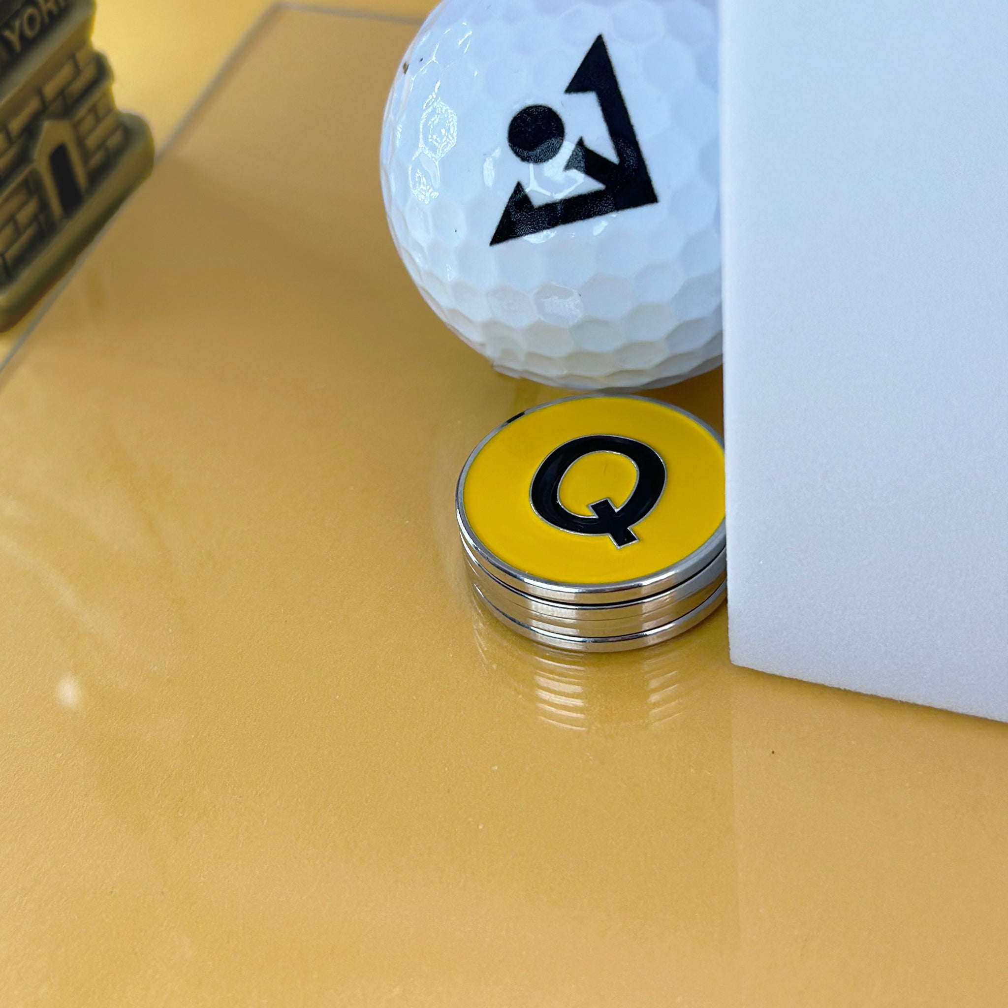 Q Train logo magnetic golf ball marker, with Statue of Liberty in a gold backdrop.
